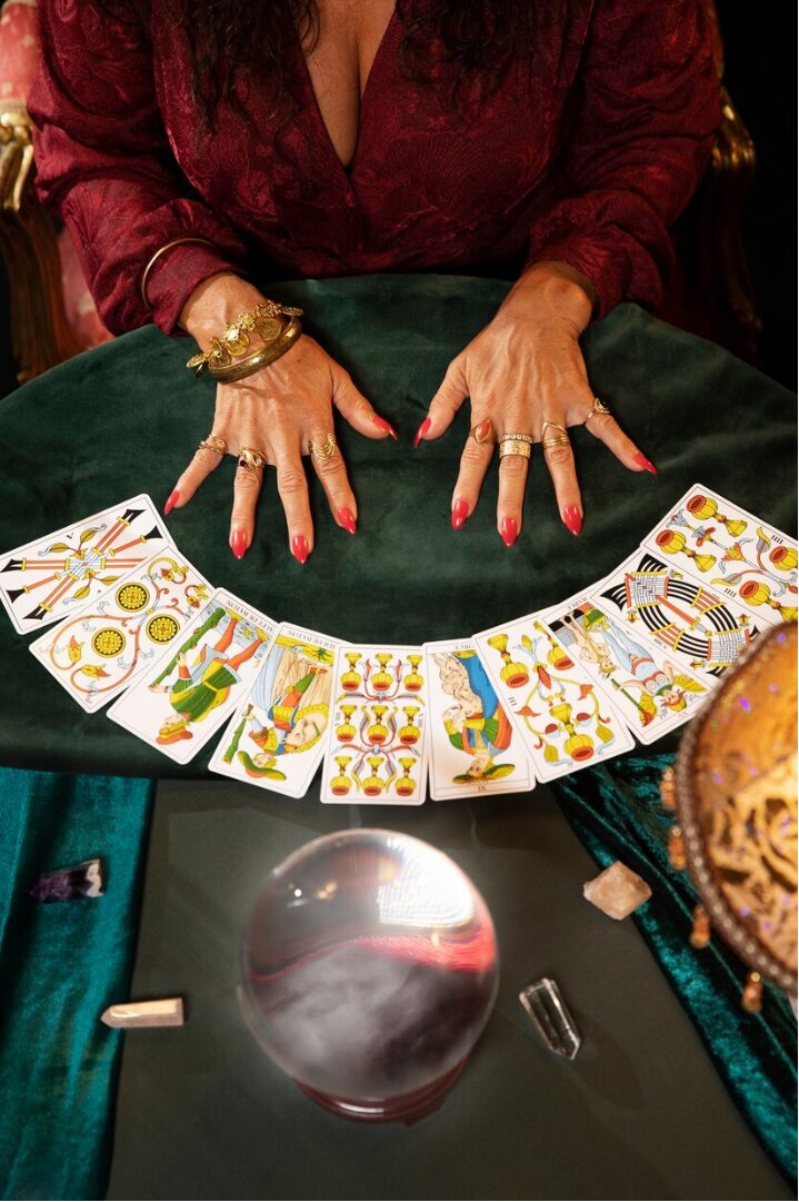 Una persona sentada en el está realizando una tirada de cartas de Tarot de Marsella sobre una mesa de madera. Las cartas están dispuestas en un diseño tradicional, con algunas cartas boca arriba, revelando ilustraciones clásicas como La Rueda de la Fortuna y El Mago. Cristales y velas encendidas acompañan la sesión, sugiriendo una atmósfera de introspección y descubrimiento personal.